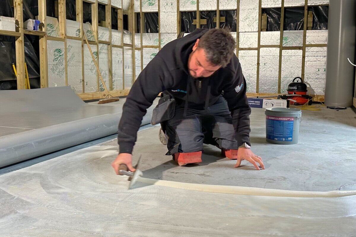 Fitter installing safety flooring for a kitchen, applying adhesive