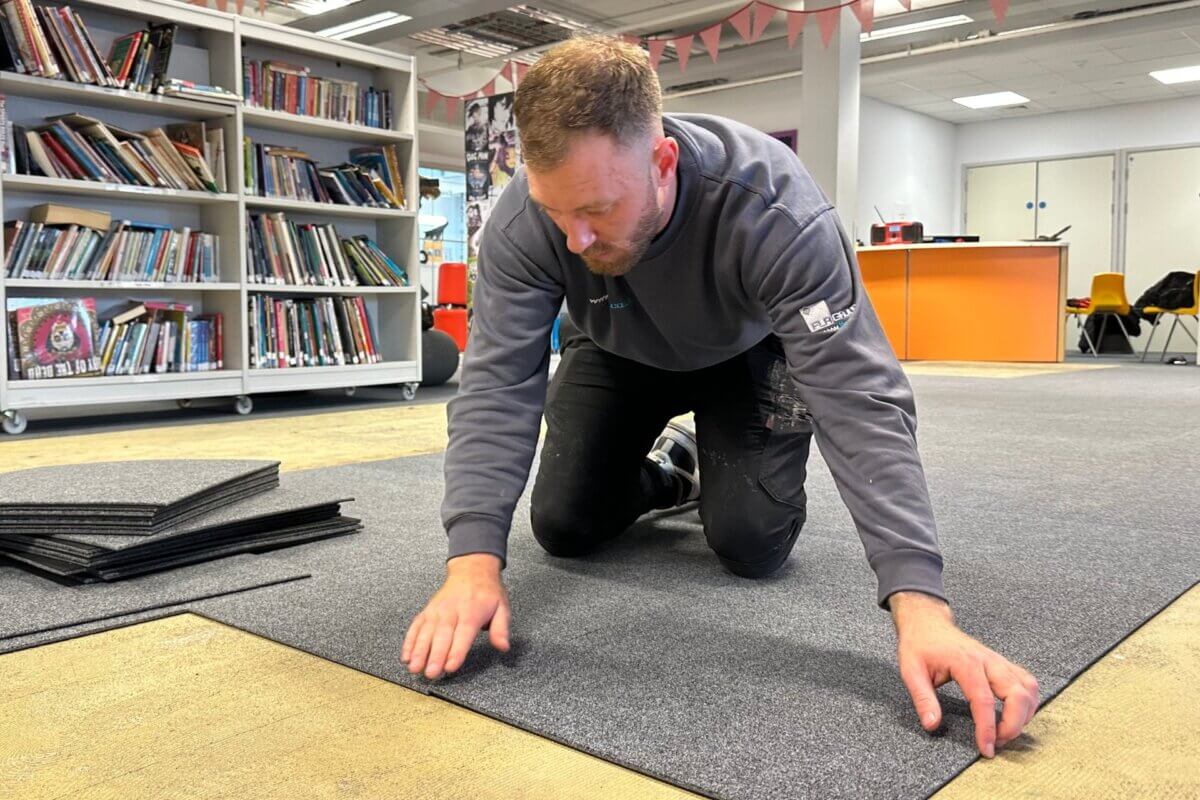 Interior shot of flooring installer fitting carpet tiles for a library at a secondary school