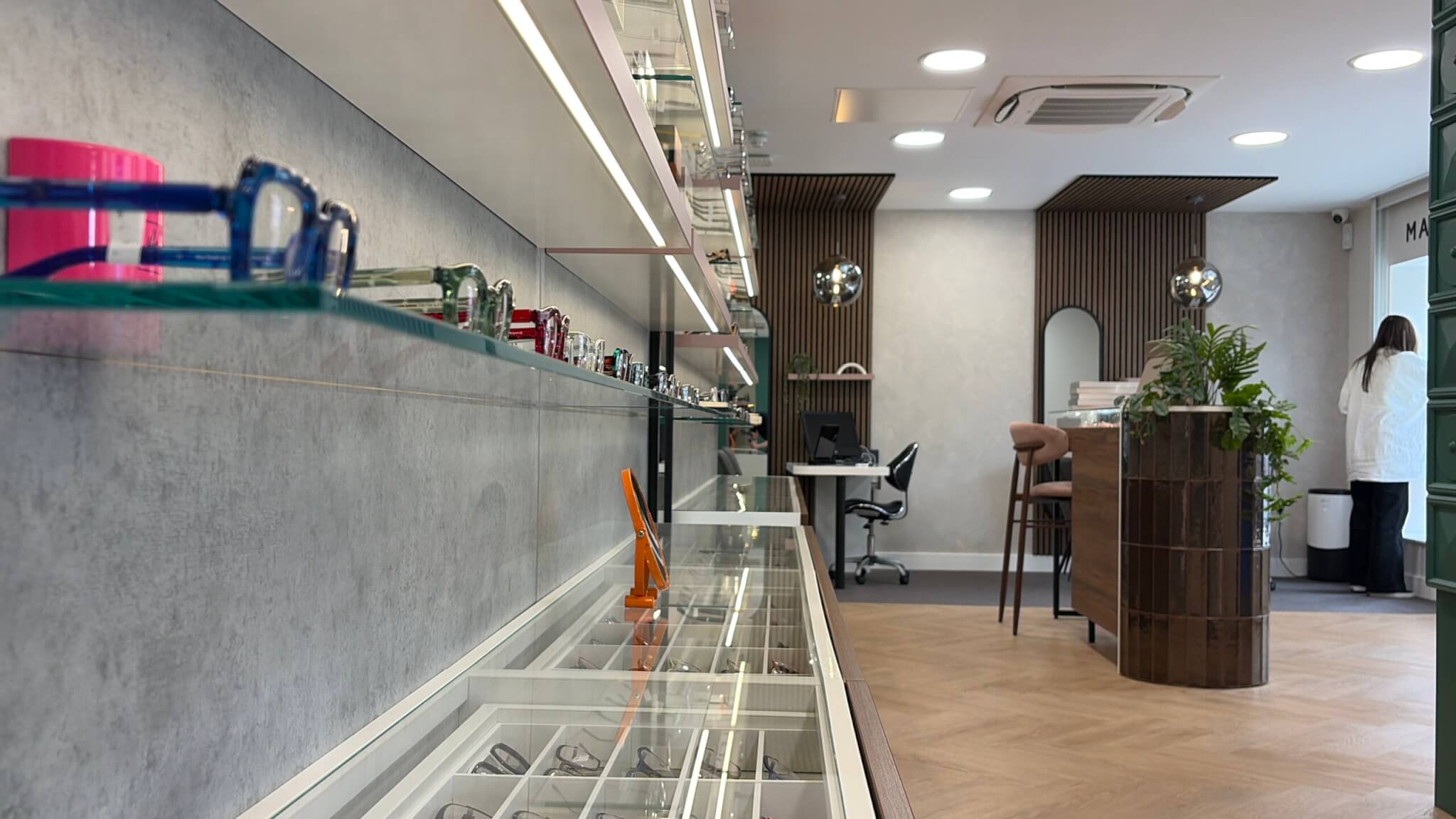 Close-up view inside Perspective Opticians in Knowle looking along a glass eyewear display cabinet, with the Plus Floor LVT in French Loft herringbone running through to the dispensing desks and service counter beyond.